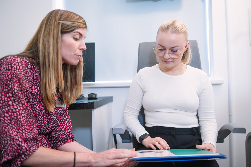 A young lady sat reading a visual test sheet with an optometrist
