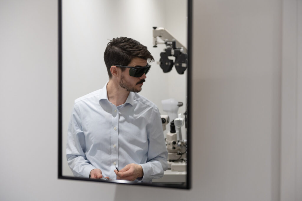 image of Matthew Carter, Director - Optometrist Independent Prescriber. The image is taken in a mirror of Matt wearing protective glasses when using a piece of equipment